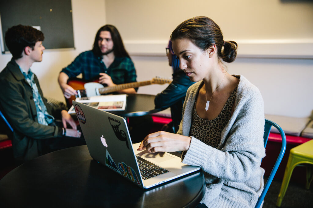 A BIMM Music student seated working at a laptop with two students behind