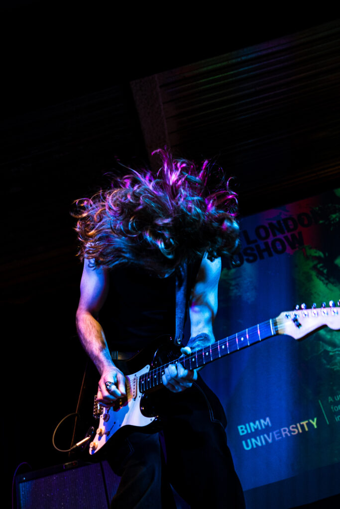 Student thrashing their head forward while playing the guitar